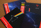 Trois vinyles japonais cultes avec OBI strips — The Dark Side of the Moon de Pink Floyd, Love Over Gold de Dire Straits et Aja de Steely Dan — disposés sur une table en bois.