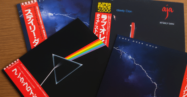 Trois vinyles japonais cultes avec OBI strips — The Dark Side of the Moon de Pink Floyd, Love Over Gold de Dire Straits et Aja de Steely Dan — disposés sur une table en bois.