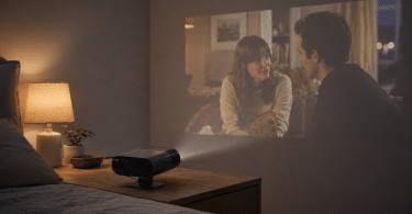 Philips NeoPix 160 Smart posé sur une table de nuit et projetant une série sur le mur d’une chambre sombre
